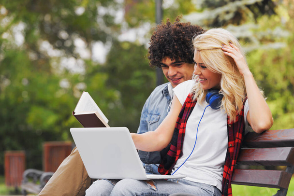 Young cheerful couple sitting on the bench studying together in the park - Foto, Imagem