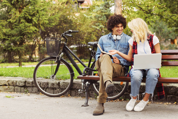 Nuori iloinen pari istuu penkillä opiskelemassa yhdessä puistossa - Valokuva, kuva