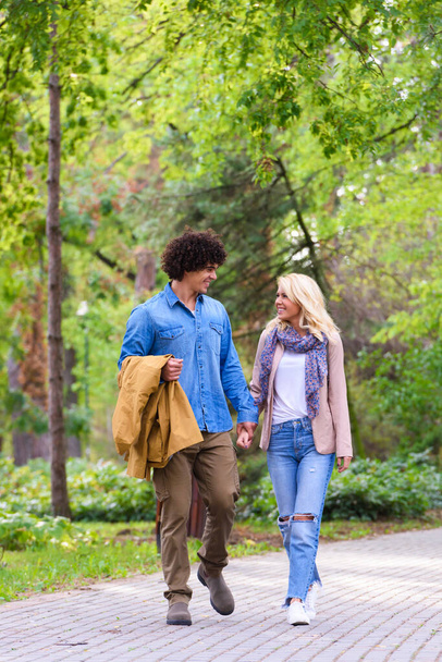 公園を歩いている若い陽気なカップルは - 写真・画像