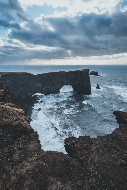A vertical high-angle shot of the sea waves crashing on the cliffs of the coastline on a cloudy day - Fotoğraf, Görsel