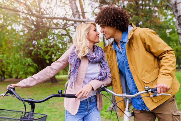 Young cheerful couple walking in the park with bicycles - Foto, imagen