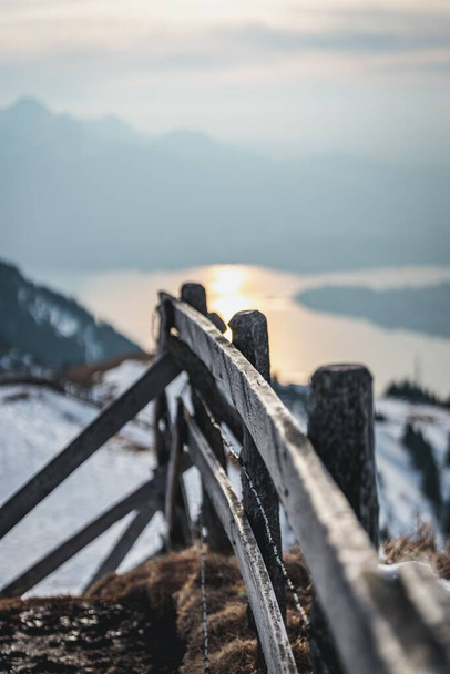 A vertical shot of a wooden fence on a snowy mountain near a river - Fotoğraf, Görsel