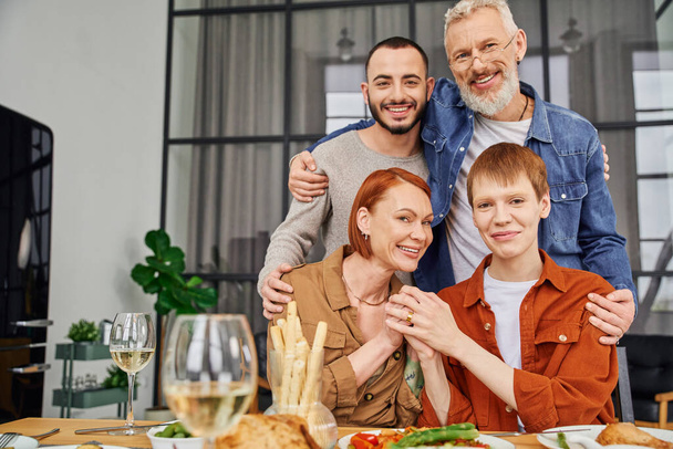 onnellinen parrakas mies halaus poika lähellä homo kumppani pöydän vieressä tarjoillaan illallinen - Valokuva, kuva