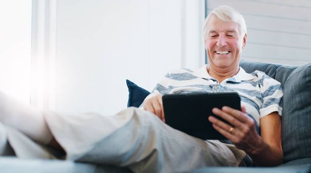 Mantenerse al día durante su retiro. un hombre mayor usando una tableta digital en el sofá en casa - Foto, Imagen
