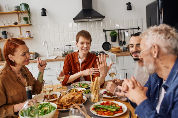 Ευτυχισμένος γκέι άντρας που δείχνει τη βέρα στους γονείς κατά τη διάρκεια του οικογενειακού δείπνου στην κουζίνα - Φωτογραφία, εικόνα