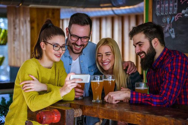 Des amis au bar buvant de la bière regardant dans le smartphone - Photo, image