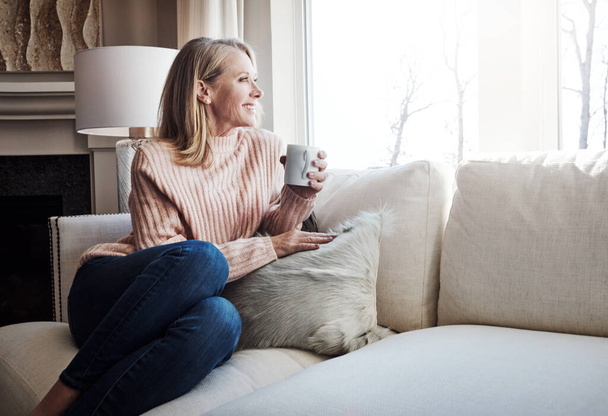 Relaxation sponsored by coffee. a mature woman relaxing on the sofa at home with a cup of coffee - Fotó, kép