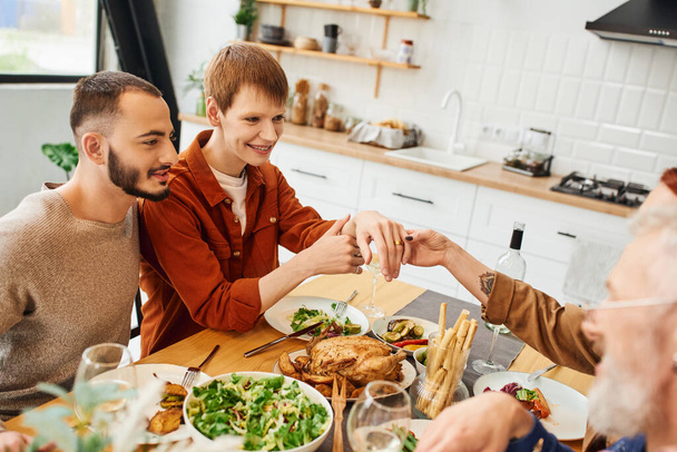 pleased gay man showing wedding ring during family dinner with boyfriend and parents in kitchen - Foto, immagini