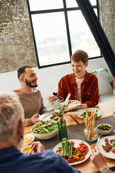 pelirroja mirando a los padres mientras sirve ensalada cerca de la pareja gay durante la cena familiar - Foto, Imagen