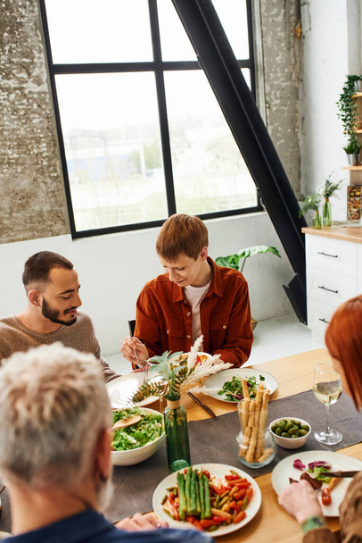 ゲイのパートナーと家族の夕食を持っている赤毛の男と現代のキッチンでぼやけた両親の高い角度ビュー - 写真・画像