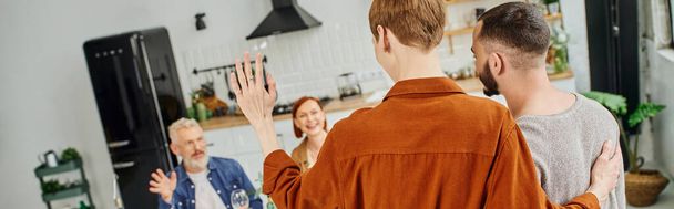 giovane uomo che abbraccia il partner gay e agita la mano ai genitori felici in cucina, banner - Foto, immagini