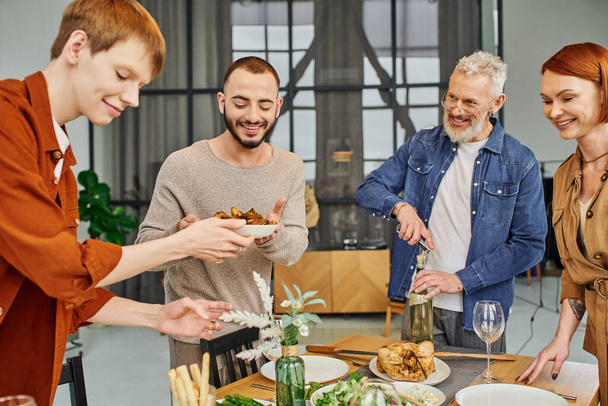cheerful gay couple serving grilled vegetables near father opening wine in kitchen - Foto, imagen