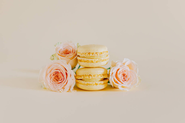 Вкусные желтые французские макароны с нежными розовыми цветками на персиковом фоне. Место для текста. - Фото, изображение
