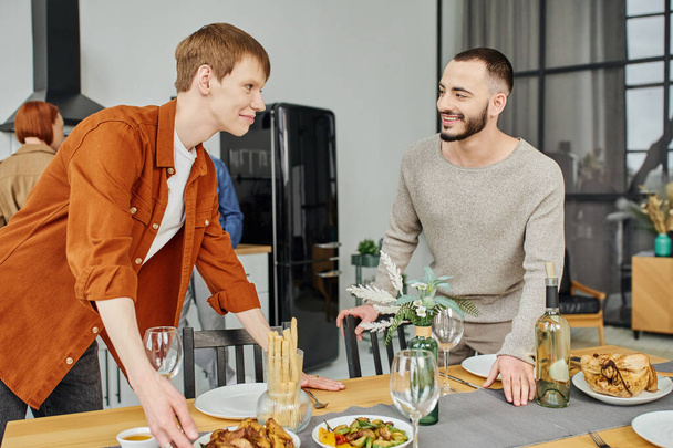 happy gay couple looking at each other near prepared supper in modern kitchen - Zdjęcie, obraz