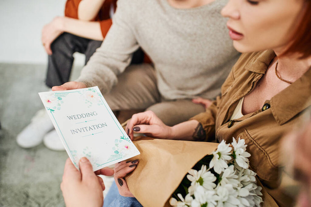 cropped view of shocked woman with flowers looking at wedding invitation near young gay couple - Фото, изображение