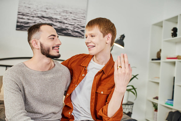 cheerful redhead gay man showing wedding ring near bearded boyfriend at home - Fotografie, Obrázek