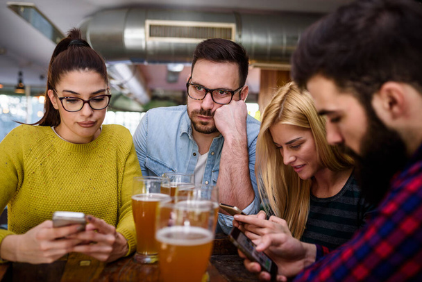 Friends at the bar drinking beer with smartphones - Fotoğraf, Görsel