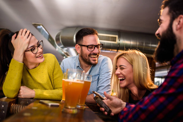 Přátelé v baru popíjejí pivo s chytrými telefony - Fotografie, Obrázek