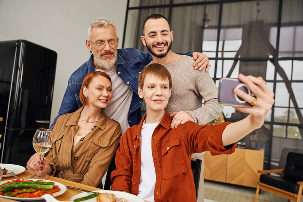 Рыжий гей делает селфи со счастливыми родителями и парнем во время семейного ужина дома - Фото, изображение