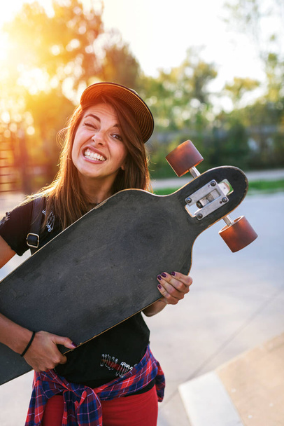 Χαριτωμένο κορίτσι της πόλης κρατώντας longboard στο πάρκο skate - Φωτογραφία, εικόνα