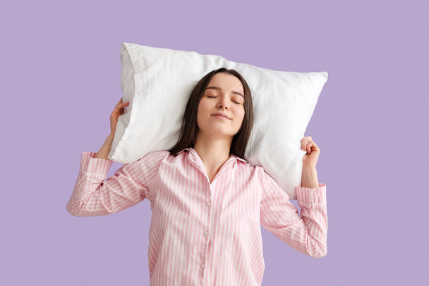 Young woman with soft pillow on lilac background - Fotoğraf, Görsel