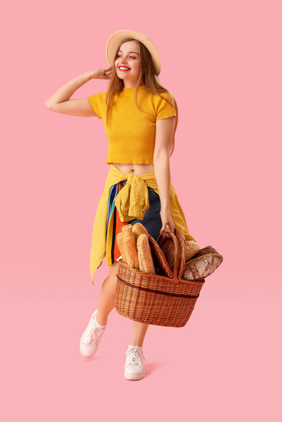 Young woman in hat with basket of fresh bread on pink background - Photo, image