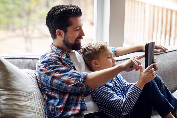 Opetat hänen pojalleen kaiken ihanasta langattomasta maailmasta. pieni poika käyttää digitaalista tablettia isänsä kanssa kotona - Valokuva, kuva