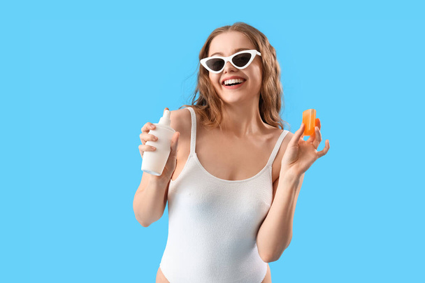 Beautiful young woman with sunscreen cream on blue background - Fotoğraf, Görsel