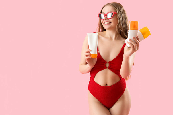 Belle jeune femme avec des crèmes solaires sur fond rose - Photo, image