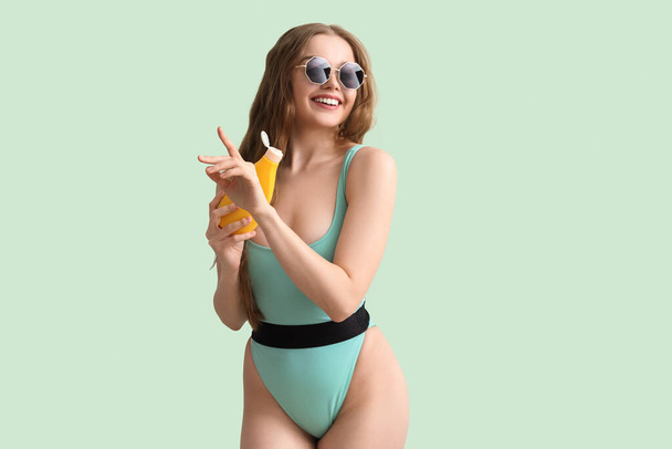 Красива молода жінка з сонцезахисним кремом на зеленому фоні
 - Фото, зображення