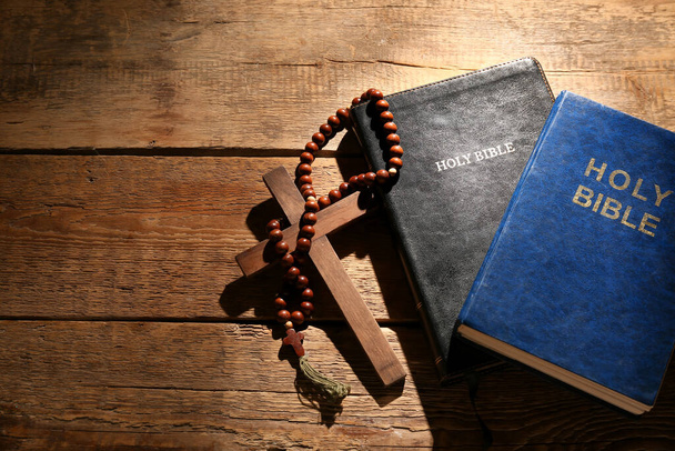 Holy Bibles with prayer beads and cross on wooden background - 写真・画像