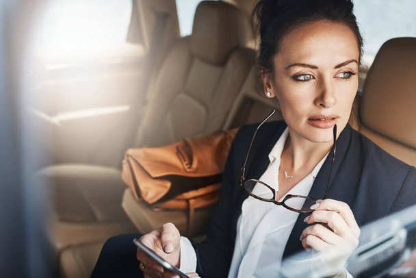 She thinks about work all the time. a confident young businesswoman seated in a car as a passenger while texting on her phone and looking outside the window on her way to work - Photo, image