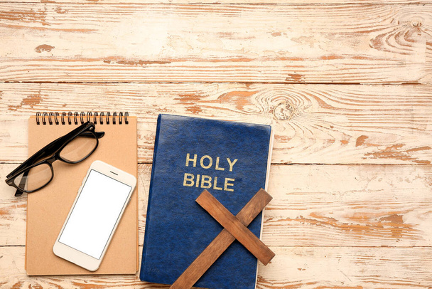 白い木製の背景に十字架、携帯電話、眼鏡とノートブックを持つ聖書 - 写真・画像