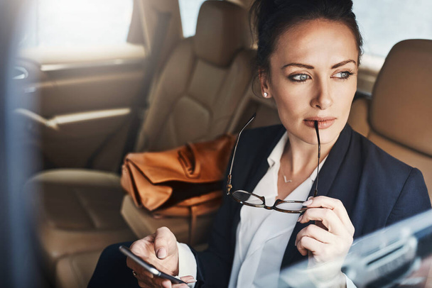 She has a great idea to share in the office. a confident young businesswoman seated in a car as a passenger while busy on her phone and looking out of the window - Foto, imagen