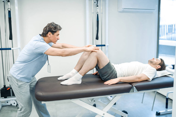 Legs rehabilitation. Male physical therapist working with patients legs - Foto, afbeelding
