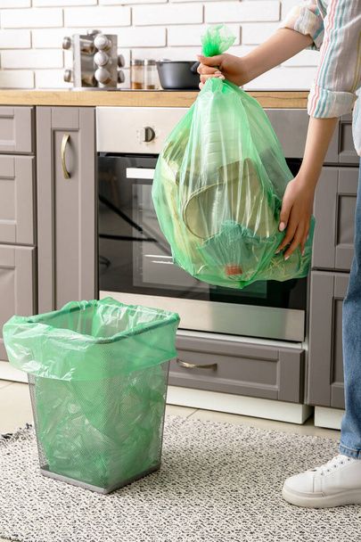 Mutfaktaki çöp kutusunun yanında dolu bir çöp torbası tutan kadın. - Fotoğraf, Görsel