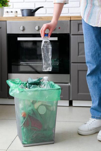 Woman putting plastic bottle into trash bin in kitchen - Foto, Imagen