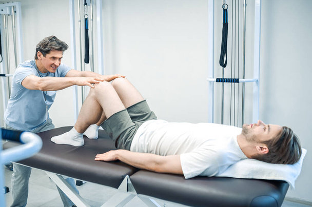 Legs rehabilitation. Male physical therapist working with patients legs - Foto, Bild