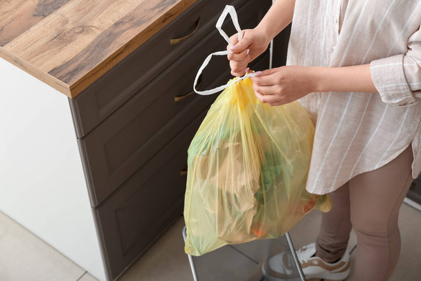 Woman holding full garbage bag near trash bin in kitchen - Valokuva, kuva