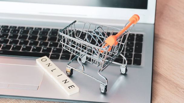 Online shopping concept. Shopping cart or trolley and laptop on wooden table - Foto, Imagen