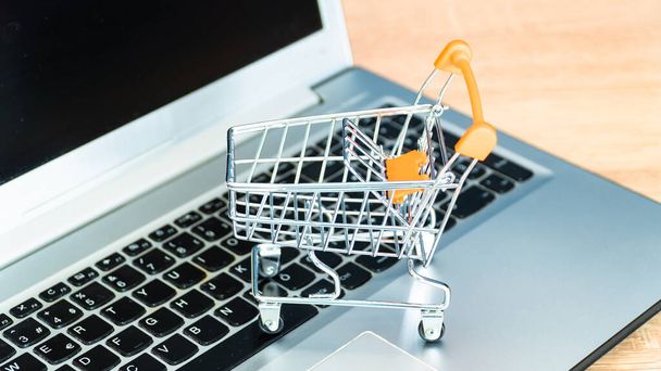 Online shopping concept. Shopping cart or trolley and laptop on wooden table - Valokuva, kuva