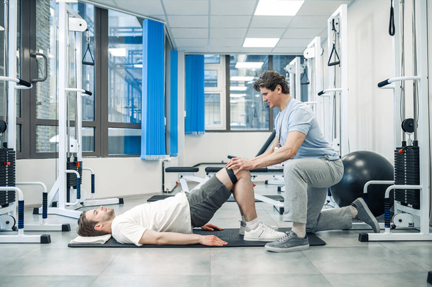 Rehabilitation. Experienced instructor assisting a man in a rehabilitation workout - Foto, Imagen