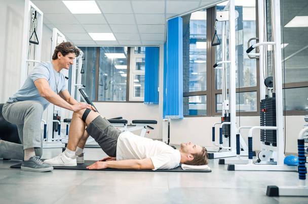 Rehabilitation. Experienced instructor assisting a man in a rehabilitation workout - Photo, image