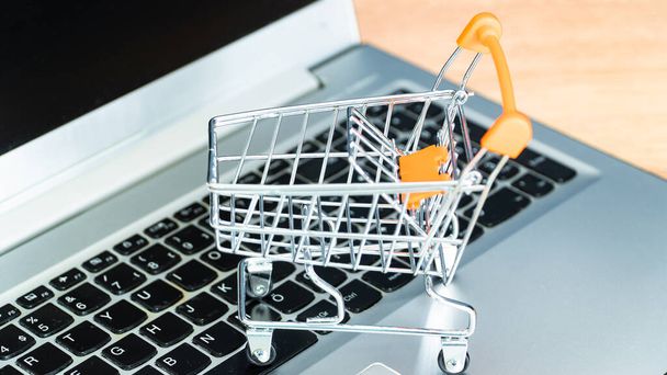Online shopping concept. Shopping cart or trolley and laptop on wooden table - Φωτογραφία, εικόνα