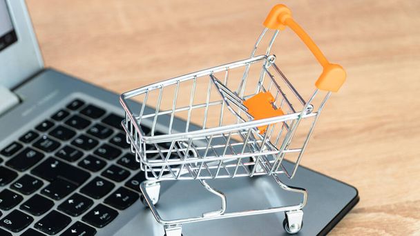 Online shopping concept. Shopping cart or trolley and laptop on wooden table - Photo, Image