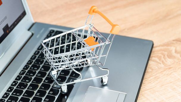 Online shopping concept. Shopping cart or trolley and laptop on wooden table - Fotó, kép