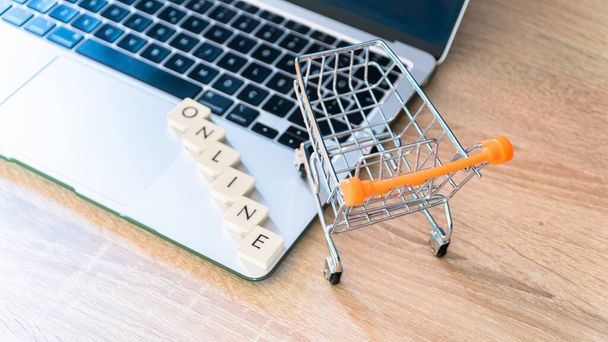 Online shopping concept. Shopping cart or trolley and laptop on wooden table - Fotó, kép