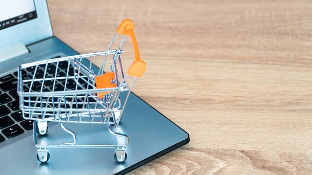 Online shopping concept. Shopping cart or trolley and laptop on wooden table - Photo, image