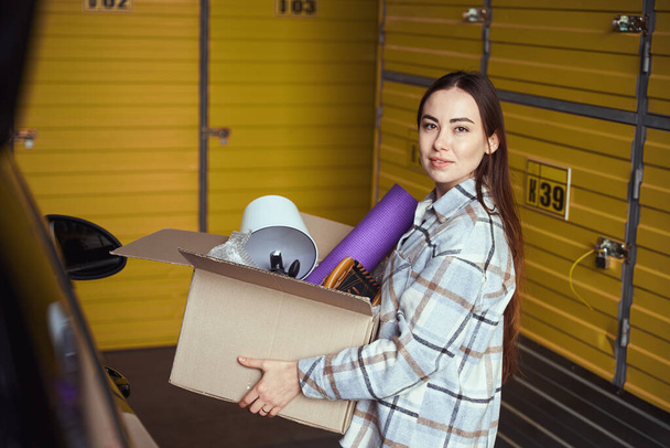 Peaceful young female keeping goods in a cardboard box while standing in the stock - Photo, Image