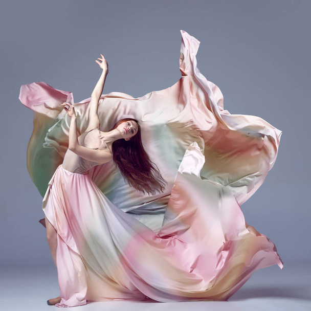 Inspired young, beautiful ballerina wearing rainbow dress dancing over grey studio background. Ballet with silk dress. Concept of classic ballet, inspiration, beauty, contemporary, dance, creativity - Photo, Image